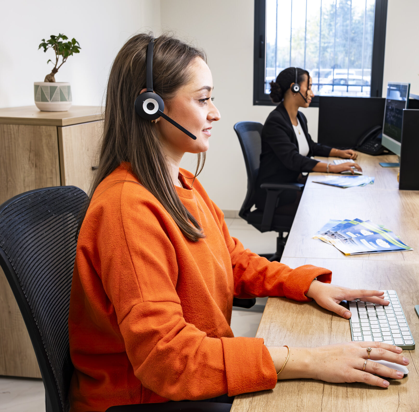 Deux conseillères en téléservice portant casques-micro, travaillant sur ordinateurs côte à côte dans un bureau lumineux.