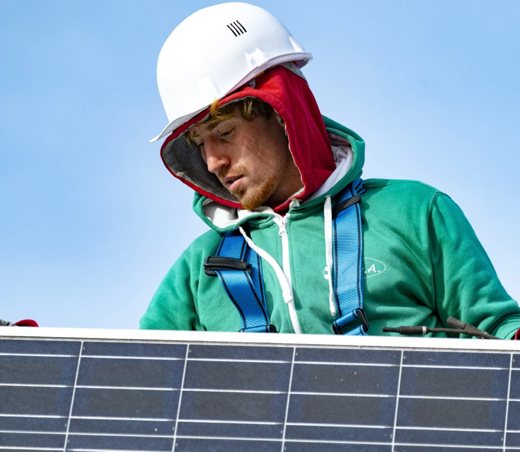 Installateur photovoltaïque en gros plan posant un panneau solaire sur toiture, casque et harnais de sécurité, pose de module solaire.