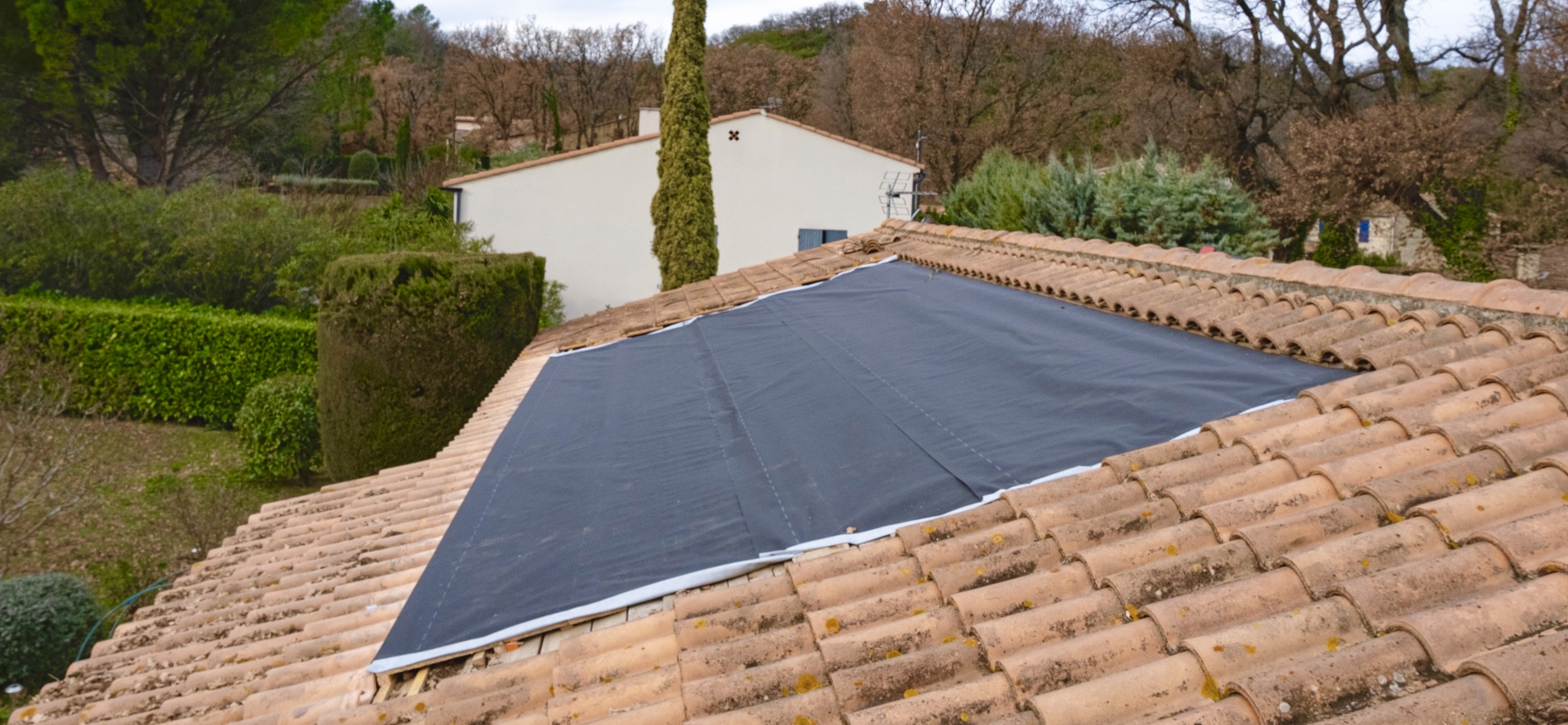 Grande bâche d’étanchéité noire tendue entre les tuiles, couvrant une large portion du toit en attente d’installation photovoltaïque.