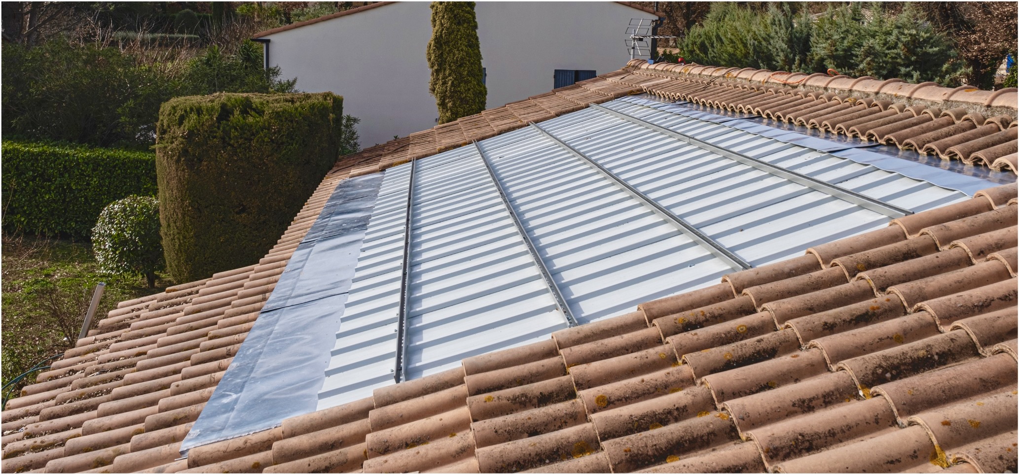 Toiture bac acier installée entre tuiles, rails de montage alignés et rive métallique avant pose des panneaux.