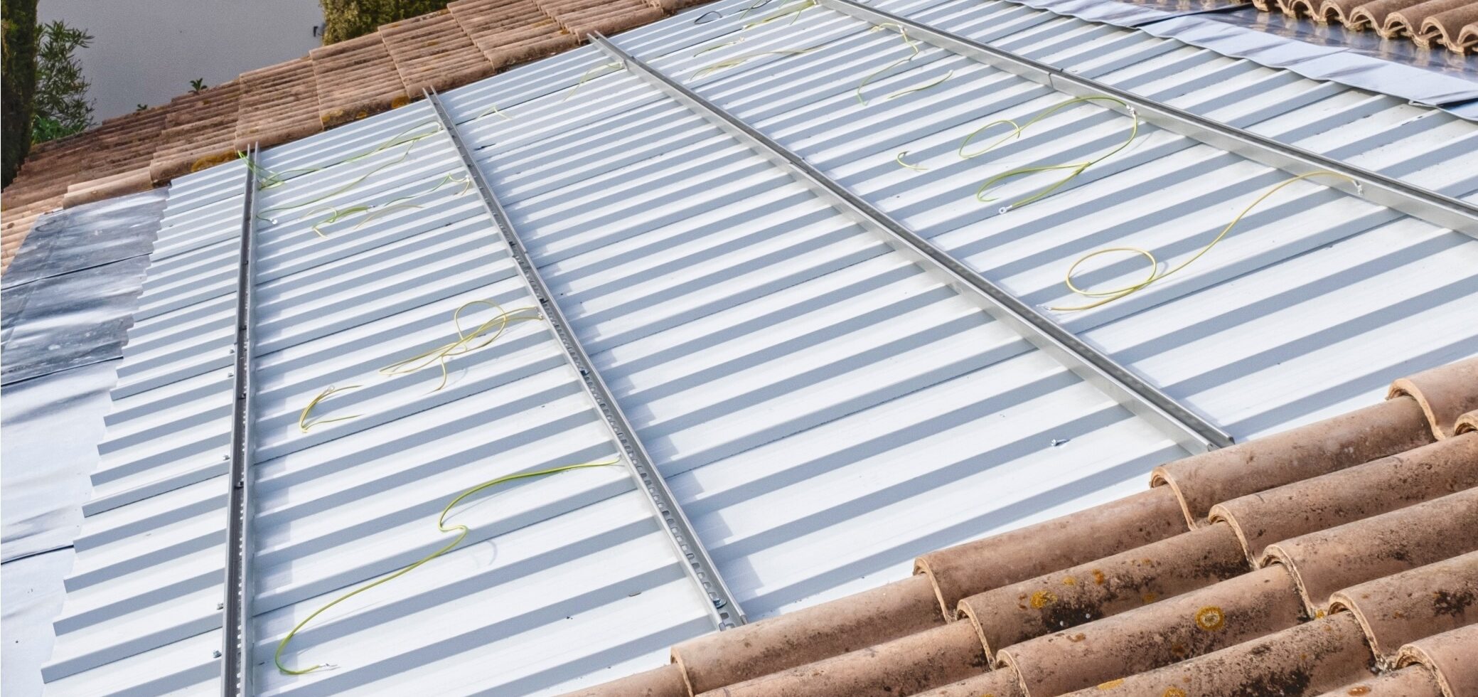 Rails de fixation posés sur une toiture bac acier, câbles vert/jaune déroulés pour la mise à la terre, tuiles en rive.