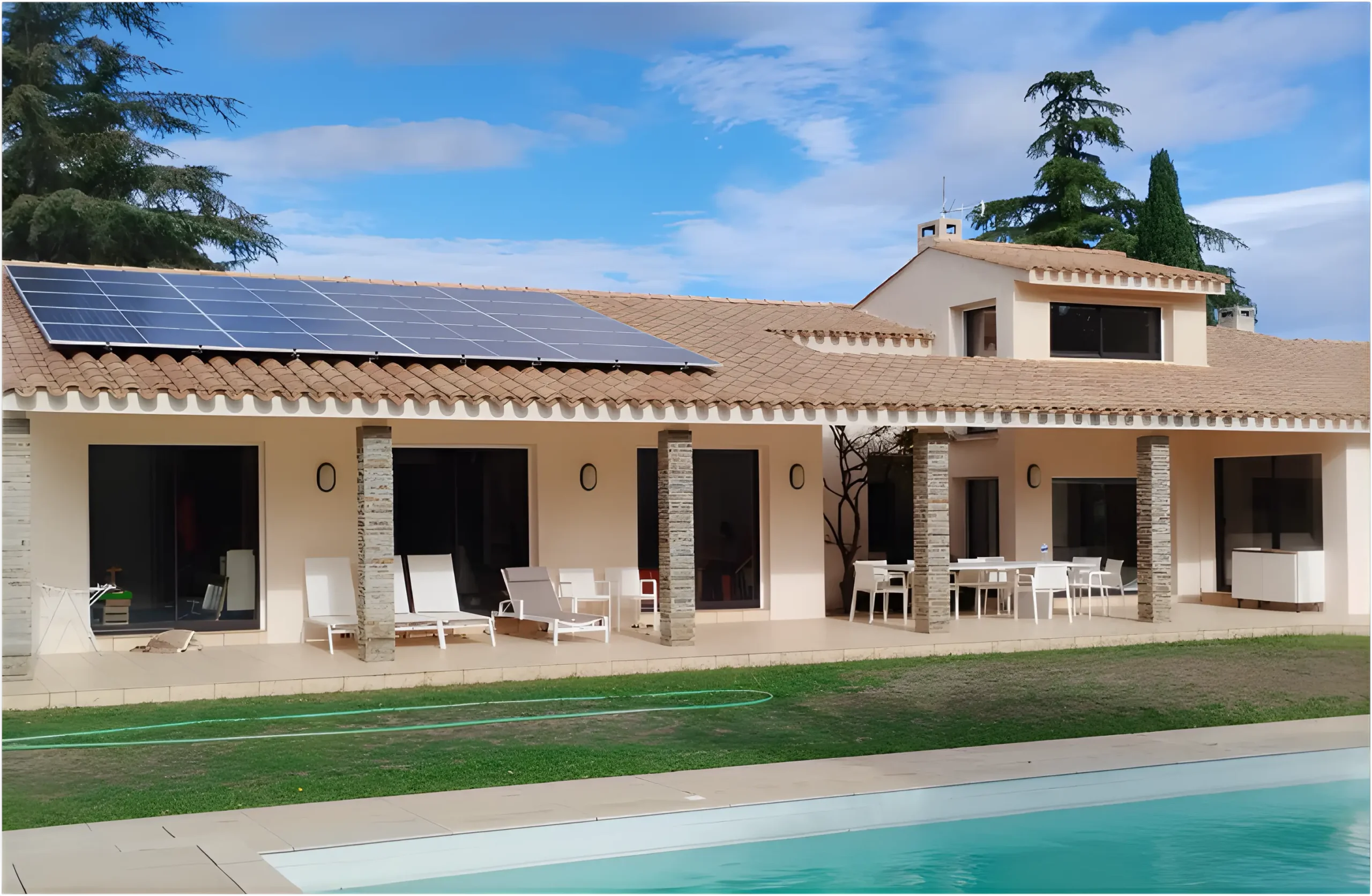 Toiture en tuiles canal d’une villa avec une rangée de panneaux photovoltaïques noirs, terrasse couverte en rez-de-jardin et piscine en premier plan sous un ciel bleu.